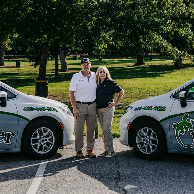 The founder and finance director pose for a picture in a green park, standing in front of two company vehicles.