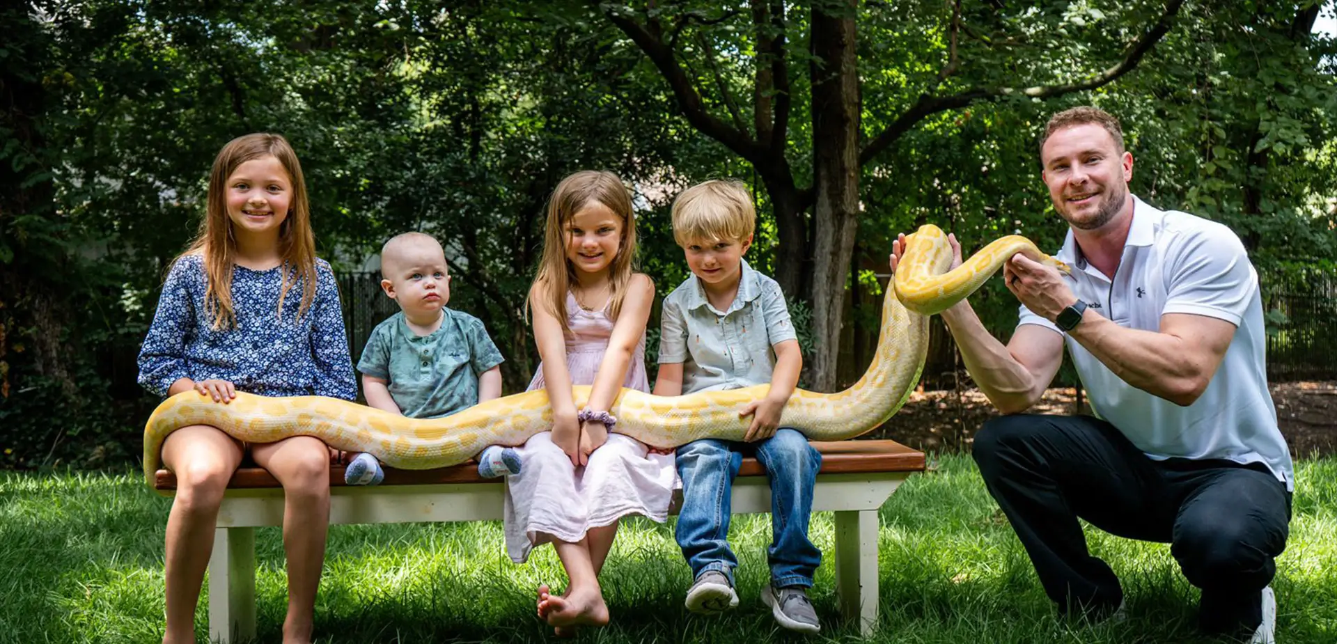 Children on a bench holding a large yellow snake with The Creature Teacher at a live animal birthday party