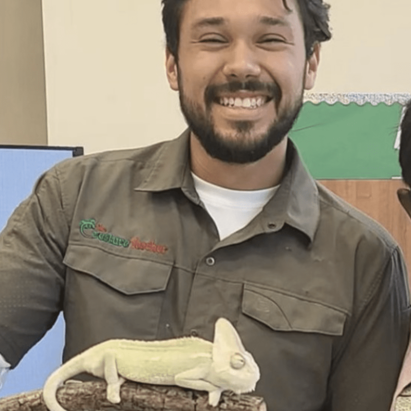 The Creature Teacher Ben smiling and holding a veiled chameleon at a live animal birthday party