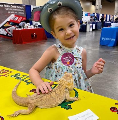 Girl smiling while petting a bearded dragon at a STEM night booth